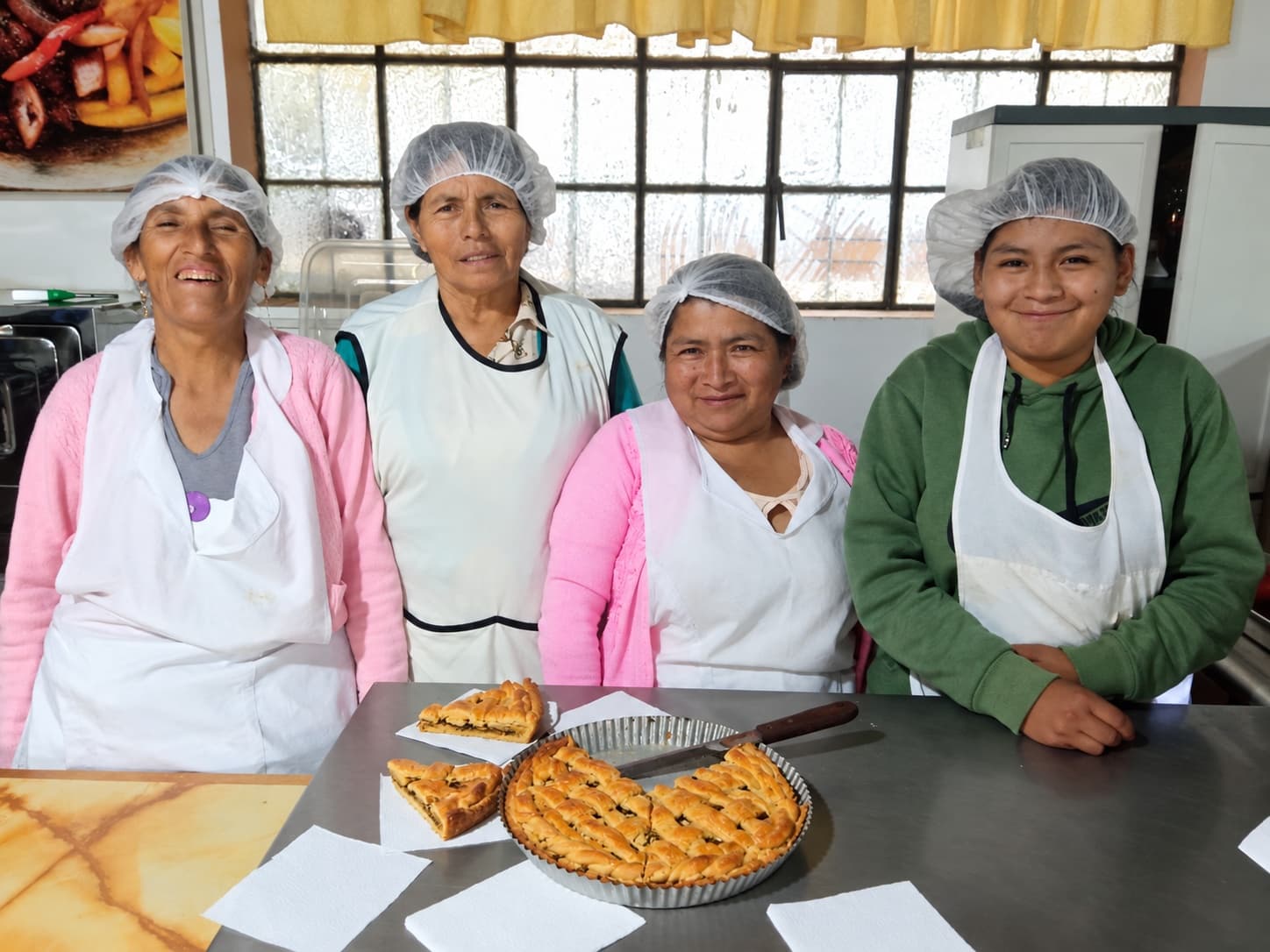 Cuatro participantes del taller de cocina y repostería posan junto a una tarta que acaban de hornear.
