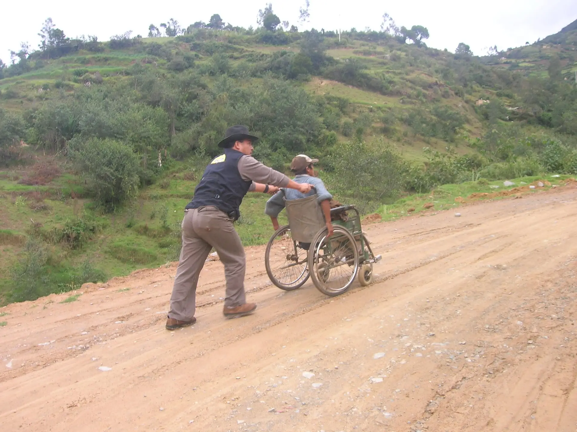 Richard acompaña a una persona en silla de ruedas por un camino rural.