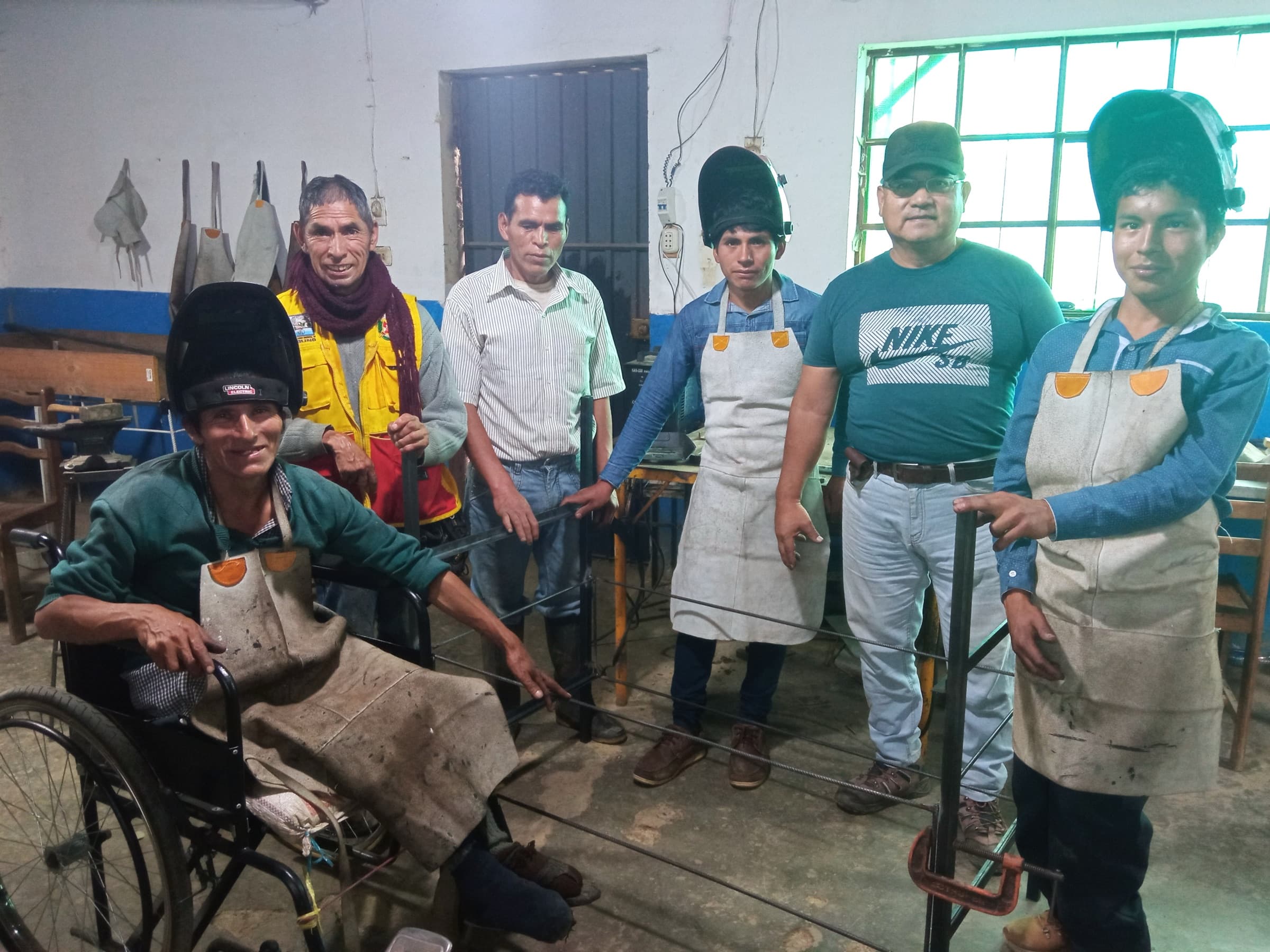 Richard junto a participantes en el taller de carpintería metálica, sosteniendo una estructura que fabricaron.